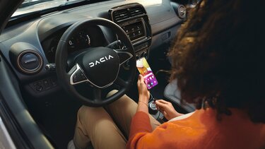 Visual Dacia interieur met vrouw met smartphone achter het stuurwiel