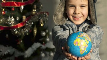 Ein Junge hält vor einem Weihnachtsbaum eine Weltkugel 