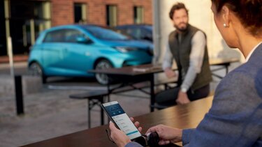 Frau am Handy, Renault ZOE im Hintergrund