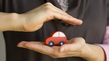 Ein rotes Holzauto in schützenden Händen 