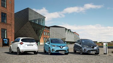 Drei Renault ZOE Fahrzeuge in weiß, blau und grau parken vor Gebäude