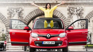 Frau mit gelbem Anzug steht in einem roten Renault mit offenem Schiebedach