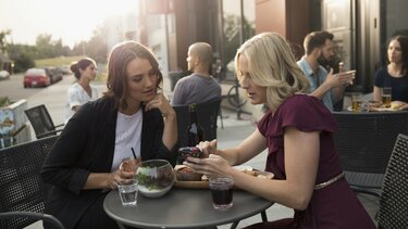 Zwei Frauen schauen sich in einem Cafe etwas auf dem Smartphone an