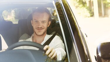 Männlicher Fahrer lächelt am Steuer seines Wagens