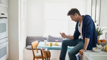 Mann sitzt auf Tischkante und blickt auf sein Handy